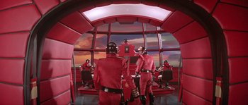 Movie still from “Flash Gordon” (1980), directed by Mike Hodges – A group of men in red uniforms standing in a room; Wide shot, Low angle