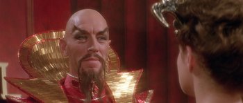 Movie still from “Flash Gordon” (1980), directed by Mike Hodges – A man with a beard and a mustache wearing a red suit; Close Up shot, Over the shoulder angle
