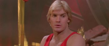 Movie still from “Flash Gordon” (1980), directed by Mike Hodges – A person with blond hair wearing a red shirt; Close Up shot, Low angle