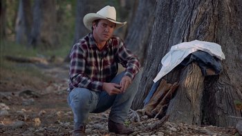 Movie still from “Flesh and Bone” (1993), directed by Steve Kloves – A man kneeling next to a tree wearing a cowboy hat; Medium shot, Over the shoulder angle