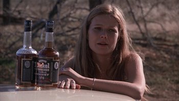 Movie still from “Flesh and Bone” (1993), directed by Steve Kloves – A woman sitting at a table with a bottle of alcohol; Close Up shot, Low angle