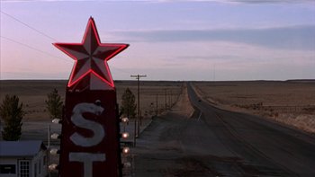 Movie still from “Flesh and Bone” (1993), directed by Steve Kloves – A red star sign sitting on the side of a road; Extreme Wide shot, Low angle