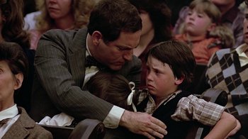 Movie still from “Footloose” (1984), directed by Herbert Ross – A man and a boy are hugging in a crowd; Medium shot, Over the shoulder angle