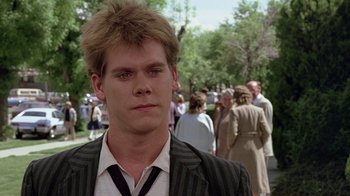 Movie still from “Footloose” (1984), directed by Herbert Ross – A man in a suit and striped tie standing in front of a group of onlookers; Close Up shot, Over the shoulder angle