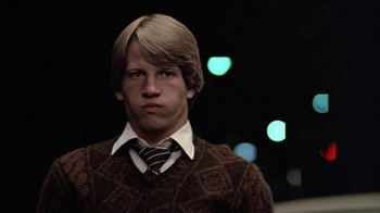 Movie still from “Footloose” (1984), directed by Herbert Ross – A young man with blonde hair wearing a sweater and a tie; Close Up shot, Low angle
