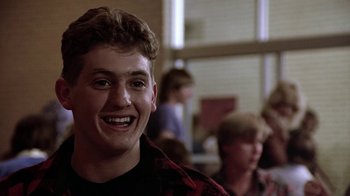Movie still from “Footloose” (1984), directed by Herbert Ross – A young man smiling at the camera in front of a group of people; Close Up shot, Low angle