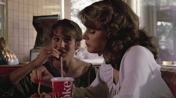 Movie still from “Footloose” (1984), directed by Herbert Ross – Two women sitting at a table with a drink in front of them; Medium shot, Over the shoulder angle
