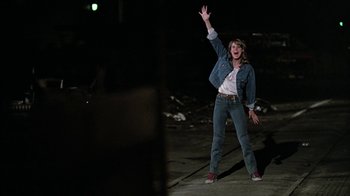 Movie still from “Footloose” (1984), directed by Herbert Ross – A woman standing on the side of a road waving; Wide shot, Low angle