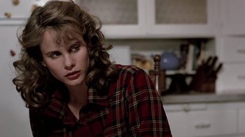 Movie still from “Footloose” (1984), directed by Herbert Ross – A woman in a red and black shirt sitting in front of a counter; Close Up shot, Over the shoulder angle