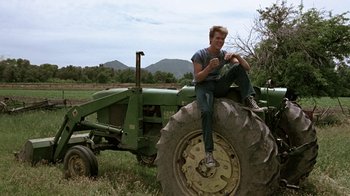 Movie still from “Footloose” (1984), directed by Herbert Ross – A man sitting on the back of a tractor; Wide shot, Low angle