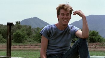Movie still from “Footloose” (1984), directed by Herbert Ross – A man sitting on the ground in front of some mountains; Medium shot, Low angle