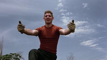 Movie still from “Footloose” (1984), directed by Herbert Ross – A man in a red shirt is jumping in the air; Medium shot, Low angle