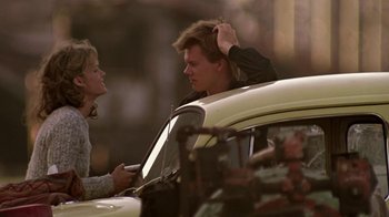 Movie still from “Footloose” (1984), directed by Herbert Ross – A man and a woman standing next to a car; Medium shot, Over the shoulder angle