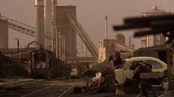 Movie still from “Footloose” (1984), directed by Herbert Ross – Two people standing next to a car in an industrial setting; Wide shot, Low angle