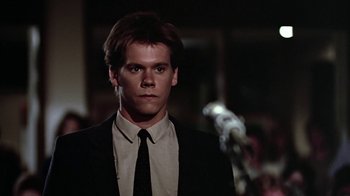 Movie still from “Footloose” (1984), directed by Herbert Ross – A man wearing a suit and tie standing in front of a microphone; Close Up shot, Low angle