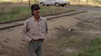 Movie still from “Footloose” (1984), directed by Herbert Ross – A man standing on the side of a road near a train track; Medium shot, Low angle