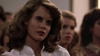 Movie still from “Footloose” (1984), directed by Herbert Ross – A woman in a white shirt is looking at the camera with another woman in the background; Close Up shot, Over the shoulder angle