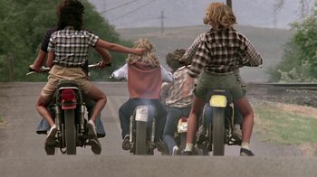 Movie still from “Footloose” (1984), directed by Herbert Ross – A group of people riding motorcycles down a street; Wide shot, Low angle