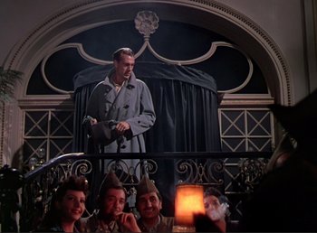 Movie still from “For Whom the Bell Tolls” (1943), directed by Sam Wood – A group of people sitting on a railing in front of a picture of a man; Wide shot, Low angle