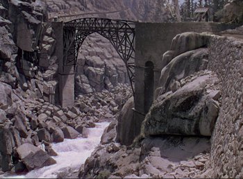 Movie still from “For Whom the Bell Tolls” (1943), directed by Sam Wood – A bridge over a river surrounded by rocks and trees; Extreme Wide shot, High angle