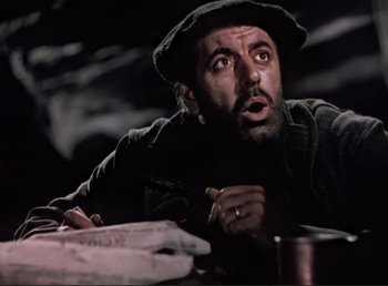 Movie still from “For Whom the Bell Tolls” (1943), directed by Sam Wood – A man with a beard and a hat is sitting at a table; Close Up shot, Low angle