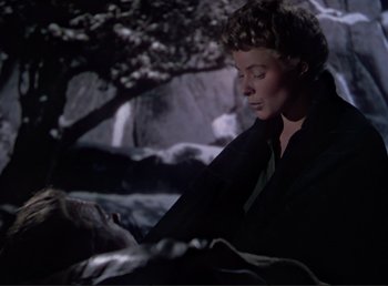 Movie still from “For Whom the Bell Tolls” (1943), directed by Sam Wood – A woman sitting on a blanket next to a tree; Medium shot, Over the shoulder angle