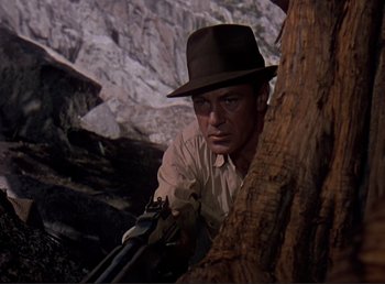Movie still from “For Whom the Bell Tolls” (1943), directed by Sam Wood – A man with a hat is holding a rifle; Medium shot, Low angle
