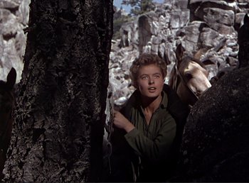 Movie still from “For Whom the Bell Tolls” (1943), directed by Sam Wood – A woman standing next to a tree with a horse behind it; Medium shot, Low angle