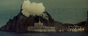 Movie still from “Force 10 from Navarone” (1978), directed by Guy Hamilton – A castle on a hill with a cloud of smoke coming out of it; Extreme Wide shot, Low angle