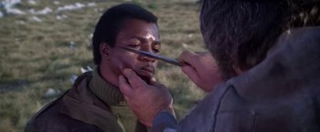 Movie still from “Force 10 from Navarone” (1978), directed by Guy Hamilton – A man is being shaved by another man outside; Close Up shot, Over the shoulder angle