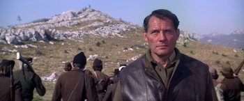 Movie still from “Force 10 from Navarone” (1978), directed by Guy Hamilton – A man in a leather vest standing in front of a group of people; Close Up shot, Low angle