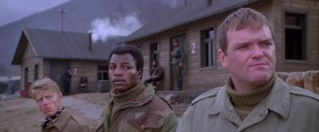 Movie still from “Force 10 from Navarone” (1978), directed by Guy Hamilton – A group of men standing in front of a building; Medium shot, Low angle