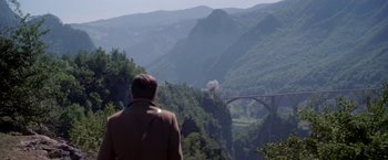 Movie still from “Force 10 from Navarone” (1978), directed by Guy Hamilton – A man standing on top of a mountain looking at a bridge; Extreme Wide shot, Over the shoulder angle