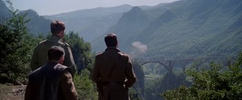 Movie still from “Force 10 from Navarone” (1978), directed by Guy Hamilton – A man standing on top of a mountain looking at a bridge; Medium shot, Low angle