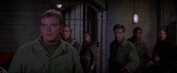 Movie still from “Force 10 from Navarone” (1978), directed by Guy Hamilton – A group of men standing next to each other in a room; Medium shot, Over the shoulder angle