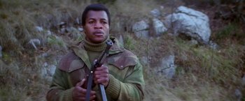 Movie still from “Force 10 from Navarone” (1978), directed by Guy Hamilton – A man holding a rifle while standing in a field; Medium shot, Low angle