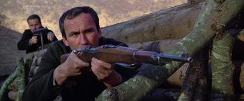 Movie still from “Force 10 from Navarone” (1978), directed by Guy Hamilton – A man holding a rifle while sitting on top of a log; Close Up shot, Low angle