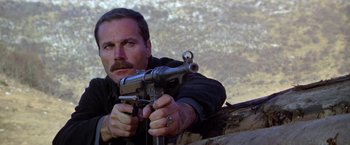 Movie still from “Force 10 from Navarone” (1978), directed by Guy Hamilton – A man holding a gun while standing next to a tree; Close Up shot, Low angle