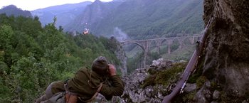 Movie still from “Force 10 from Navarone” (1978), directed by Guy Hamilton – A man standing on top of a mountain near a bridge; Extreme Wide shot, High angle