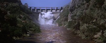 Movie still from “Force 10 from Navarone” (1978), directed by Guy Hamilton – A dam with water coming out of it; Extreme Wide shot, Low angle