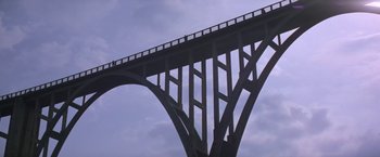 Movie still from “Force 10 from Navarone” (1978), directed by Guy Hamilton – A view looking up at a bridge with a sky background; Extreme Wide shot, Low angle