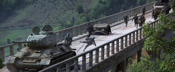 Movie still from “Force 10 from Navarone” (1978), directed by Guy Hamilton – A man falling off of a military tank on the side of a bridge; Extreme Wide shot, High angle