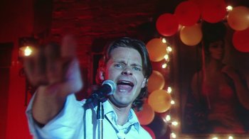 Movie still from “Forces of Nature” (1999), directed by Bronwen Hughes – A man is singing into a microphone in front of balloons; Close Up shot, Low angle