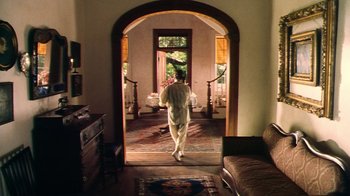 Movie still from “Forces of Nature” (1999), directed by Bronwen Hughes – A man walking through an arched doorway in a living room; Wide shot, High angle