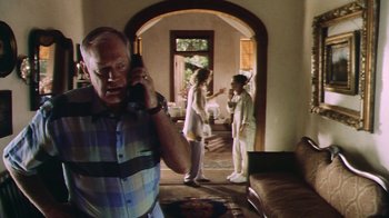Movie still from “Forces of Nature” (1999), directed by Bronwen Hughes – An older man talking on a phone while two other people stand in the background; Medium shot, Low angle