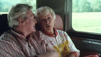 Movie still from “Forces of Nature” (1999), directed by Bronwen Hughes – An older man sitting next to an older woman on a train; Medium shot, High angle