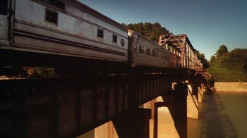 Movie still from “Forces of Nature” (1999), directed by Bronwen Hughes – A train traveling over a bridge with trees in the background; Extreme Wide shot, Low angle