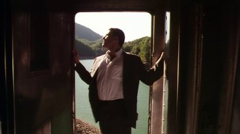 Movie still from “Forces of Nature” (1999), directed by Bronwen Hughes – A man in a suit and tie standing in front of a body of water; Medium shot, Low angle