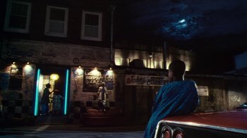 Movie still from “Forces of Nature” (1999), directed by Bronwen Hughes – A person sitting on a chair in front of a building; Extreme Wide shot, Low angle