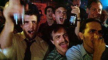 Movie still from “Forces of Nature” (1999), directed by Bronwen Hughes – A group of men sitting in front of each other holding beers; Medium shot, Low angle